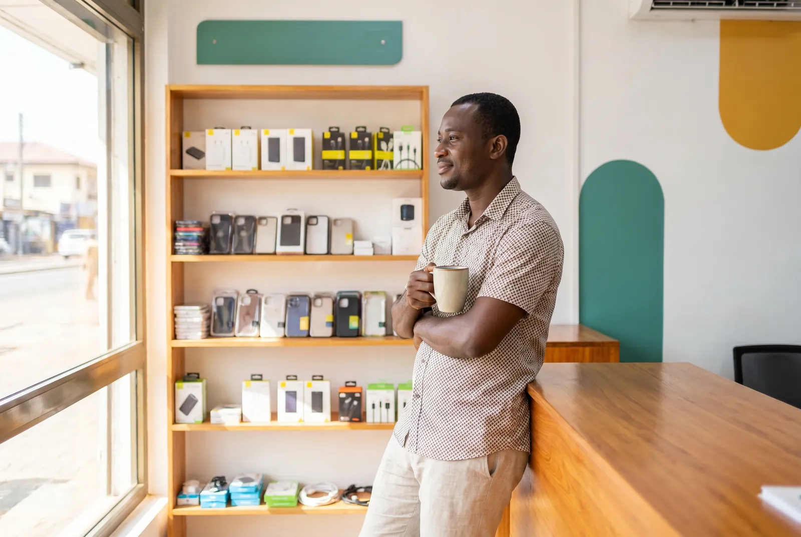 A Ghanaian electronics and phone-accessories vendor relaxed and confident, his shop running smoothly without being glued to his phone